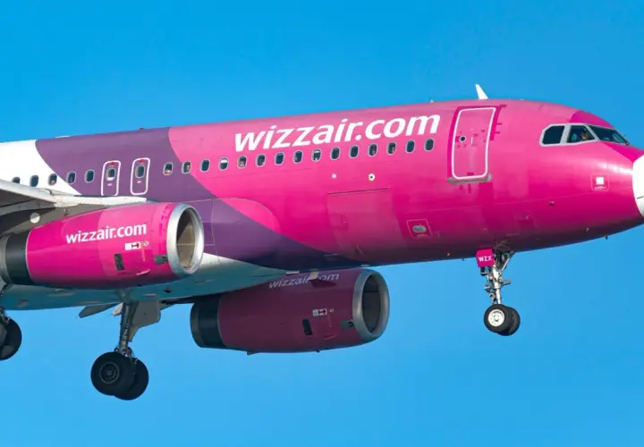 Różowy samolot Wizzair z fioletowymi elementami na tle błękitnego nieba.