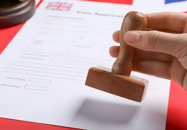 Dłoń trzyma pieczątkę nad formularzem wniosku o wizę do UK.