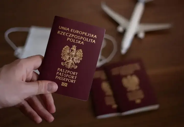 Dłoń trzyma polski paszport. Obok leżą kolejne dokumenty, maseczka i model samolotu. Zastanawiasz się, ile się czeka na paszport?