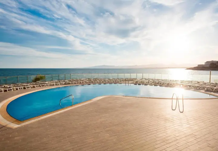 Basen przy hotelu Best Negresco z widokiem na morze i leżakami. Słońce odbija się w wodzie.
