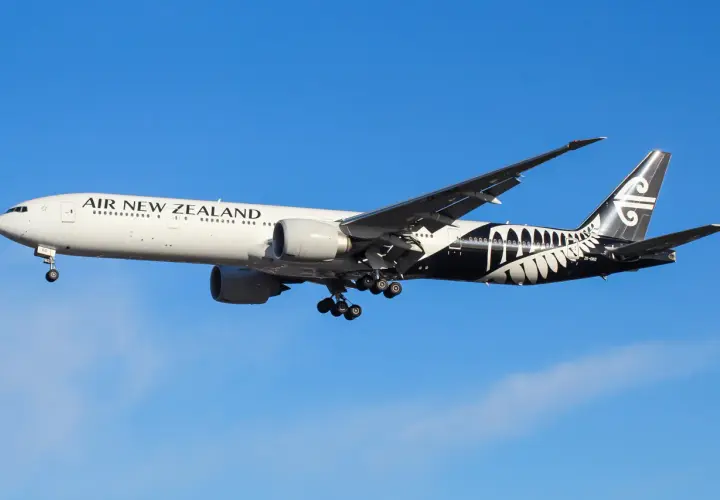 Boeing 777-200 linii Air New Zealand z charakterystycznym czarnym malowaniem z liściem paproci na ogonie, w locie na tle błękitnego nieba.