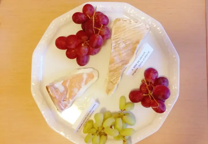 Talerz z serami Brie de Meaux i Moelleux du Revard, winogronami i etykietami, idealny do degustacji kuchni francuskiej.