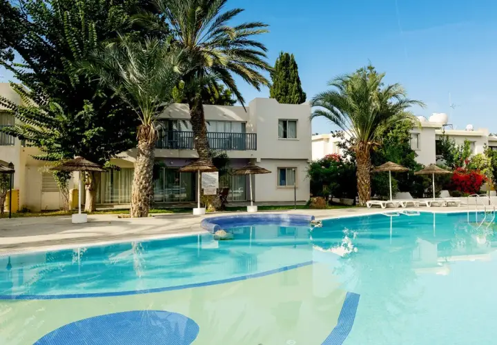 Basen w hotelu Leptos Paphos Gardens Holiday Resort, otoczony palmami i zielenią, zaprasza na relaks.
