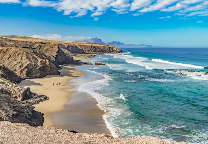 Fuerteventura pogoda sierpień: słoneczny dzień, turkusowe morze i piaszczysta plaża z klifami. Idealna pogoda na surfing.