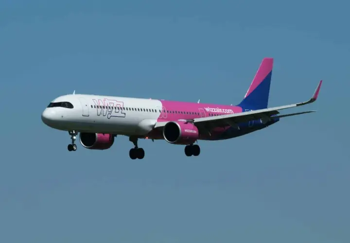 Samolot Wizz Air z różowym i niebieskim ogonem leci na tle błękitnego nieba.