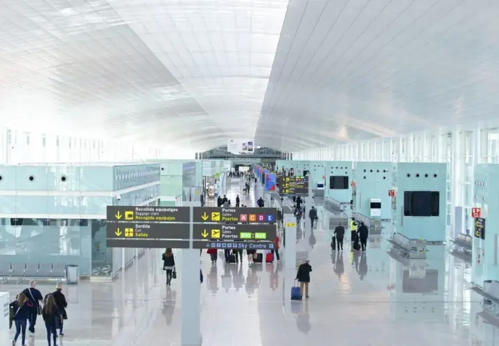 Jasny, przestronny terminal lotniska Barcelona El Prat. Pasażerowie poruszają się po nowoczesnym wnętrzu, kierując się znakami.