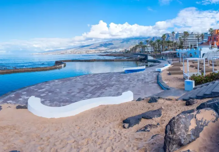 Słoneczna playa de las americas z basenem, piaskiem i kolorowymi budynkami w tle.