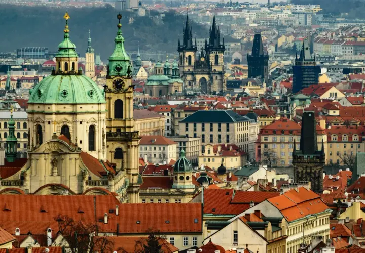 Widok panoramy Pragi z charakterystycznymi wieżami i zielonymi kopułami.