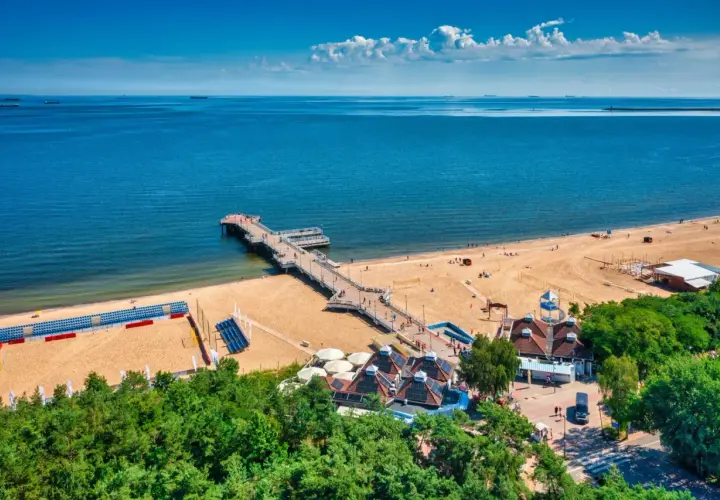 Piękny dzień na plaży w Polsce. Molo wchodzi w głąb morza, a piasek jest pełen ludzi cieszących się wakacjami.