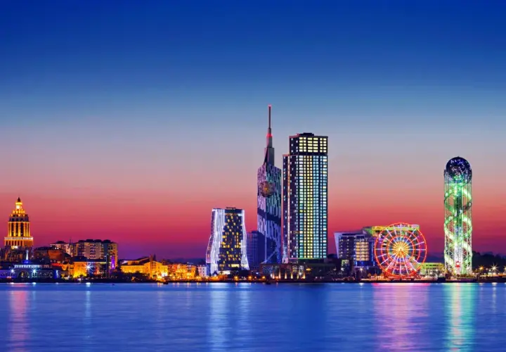 Widok na nowoczesną panoramę Batumi, stolicę Adżarii, o zachodzie słońca. Błyszczące wieżowce i diabelski młyn odbijają się w spokojnej wodzie.
