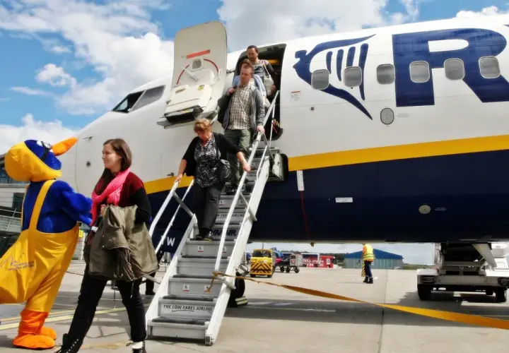 Ludzie schodzą po schodach z samolotu Ryanair, obok maskotka ptaka.