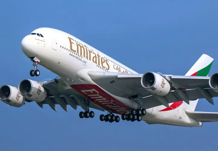 Ogromny Airbus A380 800 linii Emirates z wysuniętym podwoziem wznosi się na tle błękitnego nieba.