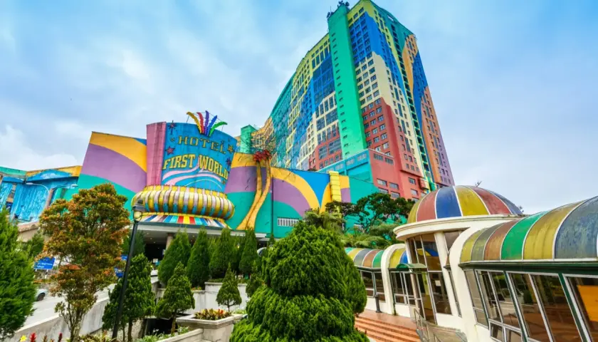 Kolorowy budynek z napisem "HOTEL FIRST WORLD" – największy hotel na świecie, otoczony zielenią i tęczowymi kopułami.