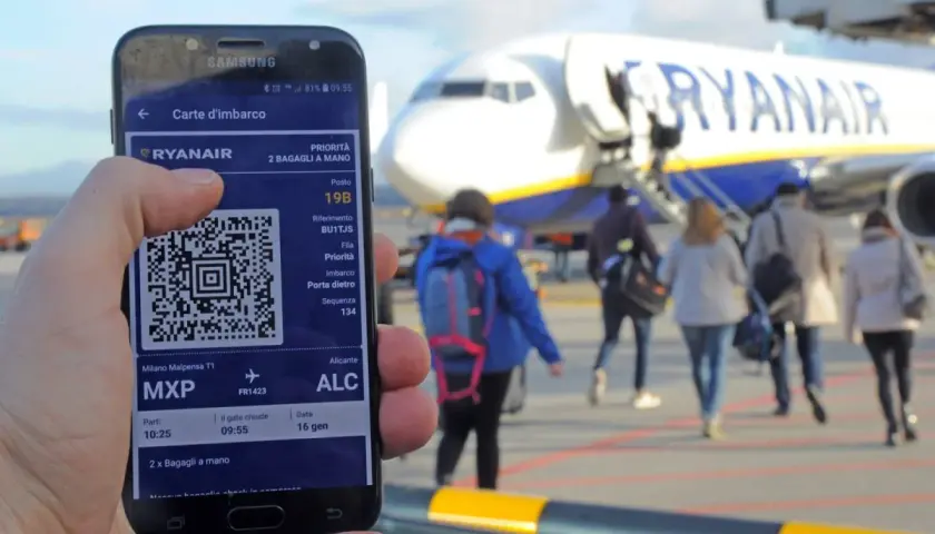 Ręka trzyma smartfon z kartą pokładową Ryanair. W tle samolot i pasażerowie.