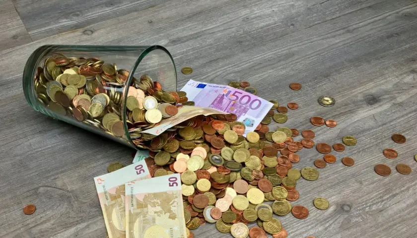 Słoik z monetami i banknotami, w tym 500 euro, rozsypany na drewnianej podłodze. To waluta Francji i innych krajów strefy euro.