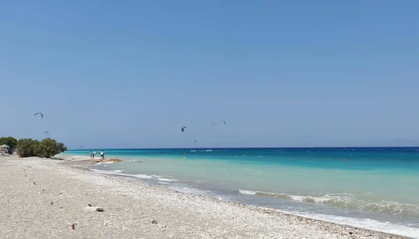 Plaża w zatoce Ialyssos, z turkusową wodą i kilkoma kitesurferami na horyzoncie.