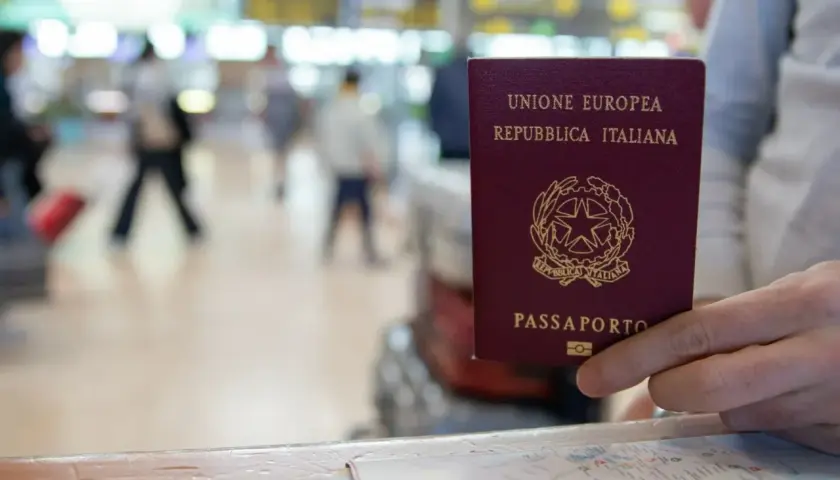 Włoski paszport w dłoni, na tle lotniska. Czy do Finlandii potrzebny jest paszport? Tak, jeśli nie jesteś obywatelem UE.