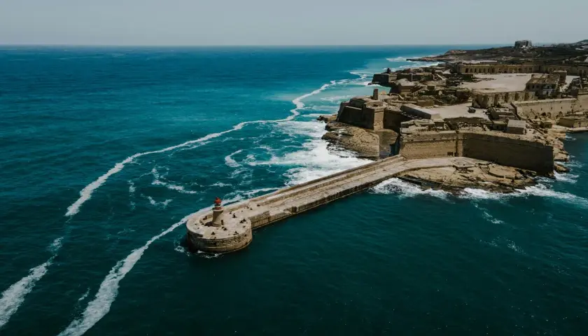 Malta: malta ile się leci? Widok na fortyfikacje i latarnię morską nad turkusowym morzem.