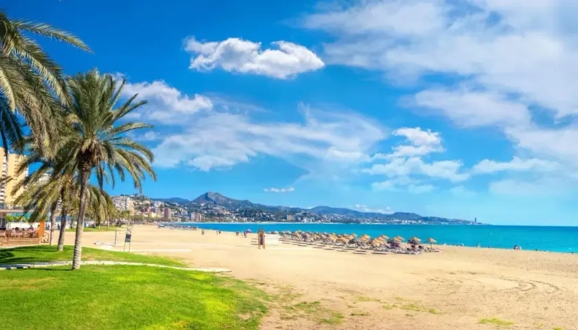Malaga w maju: słoneczna plaża z palmami, turkusowe morze i góry w tle. Idealna pogoda na wypoczynek.