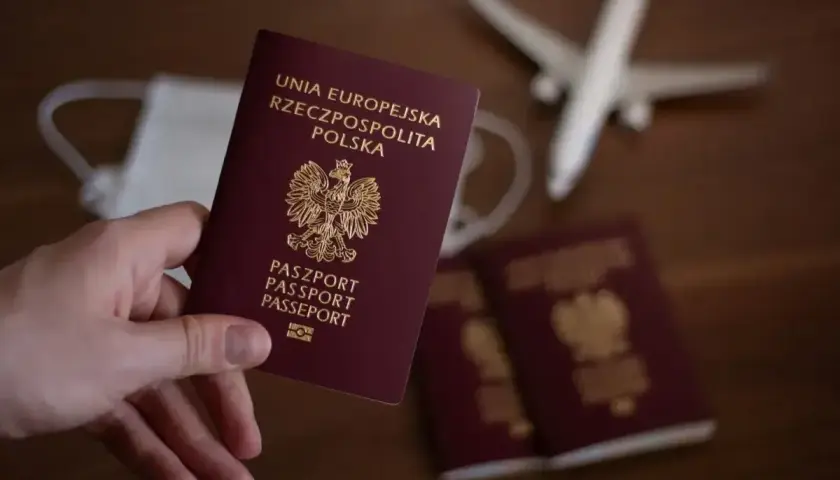 Dłoń trzyma polski paszport. Obok leżą kolejne dokumenty, maseczka i model samolotu. Zastanawiasz się, ile się czeka na paszport?