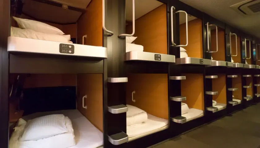 Rzędy przytulnych kapsuł w hotelu kapsułowym, każda z czystą pościelą i numerem.