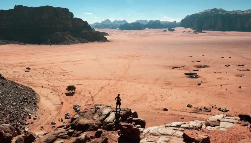 Pustynia Wadi Rum w Jordanii, gdzie turysta czeka na wizę, podziwia krajobraz z samotnym drzewem i samochodami terenowymi.