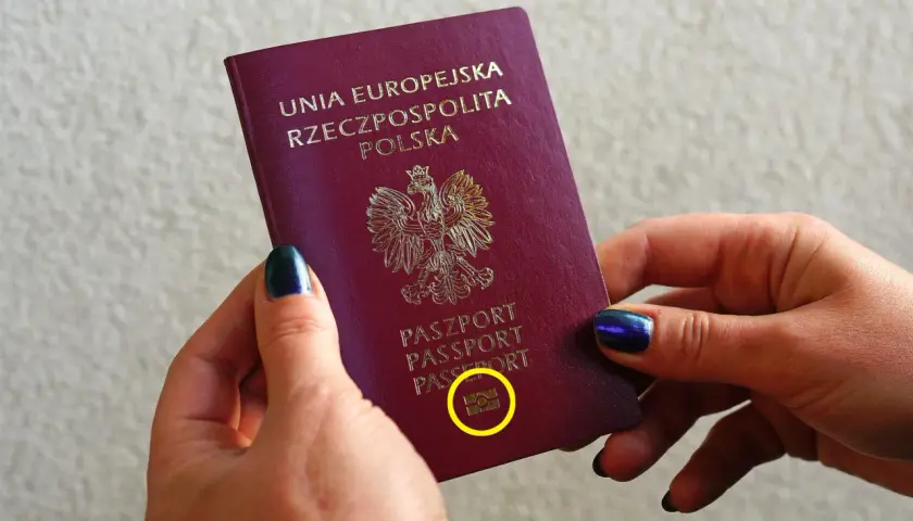Dłonie trzymają polski paszport biometryczny z symbolem aparatu.