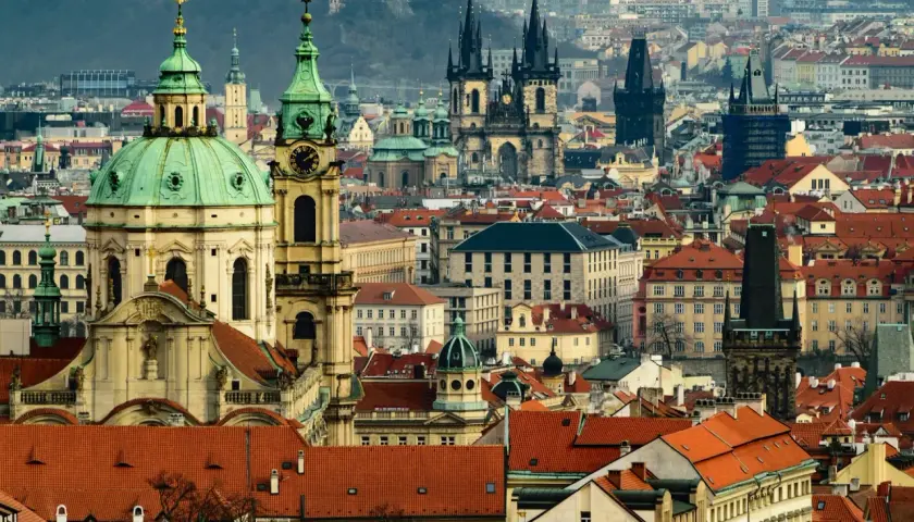 Widok panoramy Pragi z charakterystycznymi wieżami i zielonymi kopułami.