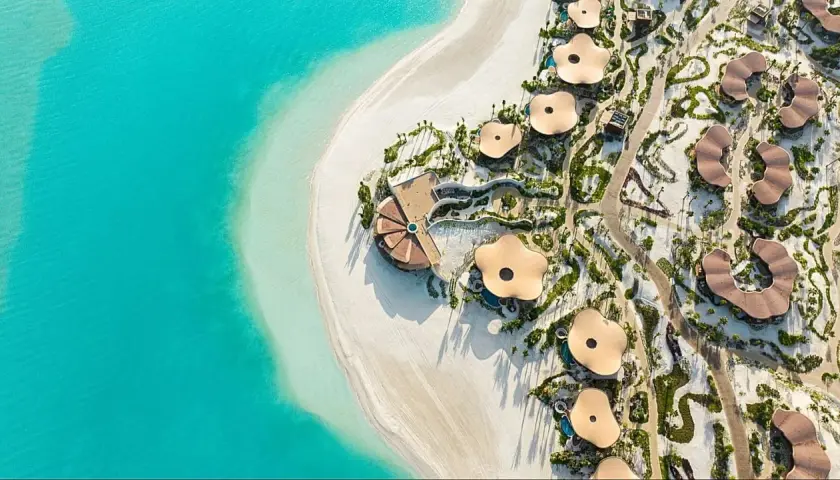 Widok z lotu ptaka na luksusowy hotel Four Seasons z unikalnymi, kwiatowymi dachami, położony przy turkusowym morzu i białej plaży.