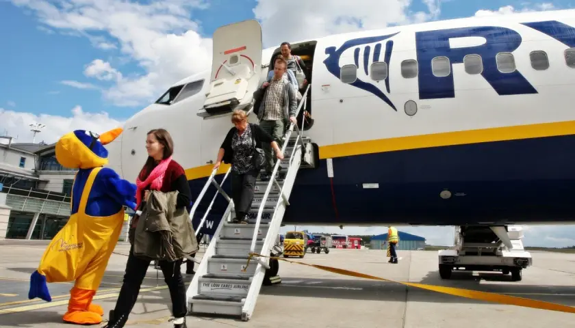 Ludzie schodzą po schodach z samolotu Ryanair, obok maskotka ptaka.