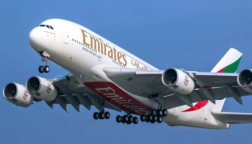 Ogromny Airbus A380 800 linii Emirates z wysuniętym podwoziem wznosi się na tle błękitnego nieba.