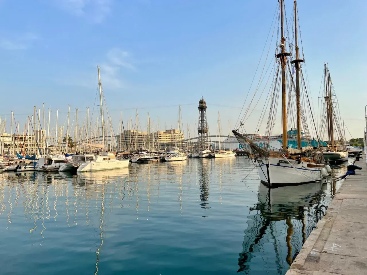 Port w Barcelonie z żaglówkami i wieżą widokową w tle.