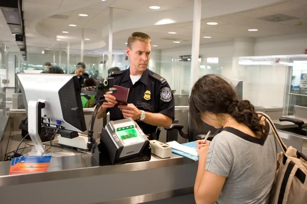 Funkcjonariusz sprawdza paszport kobiety przy stanowisku check-in na lotnisku.