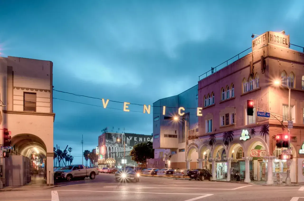 Nocny widok na Venice Beach z neonowym napisem "VENICE" i budynkami hosteli.