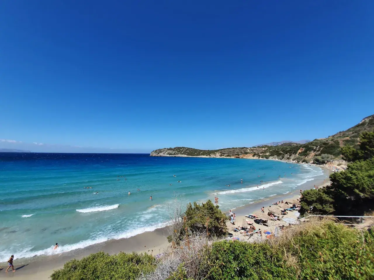 Słoneczny dzień na plaży Voulisma. Turkusowa woda, piaszczysty brzeg i zielone wzgórza tworzą idylliczny krajobraz.
