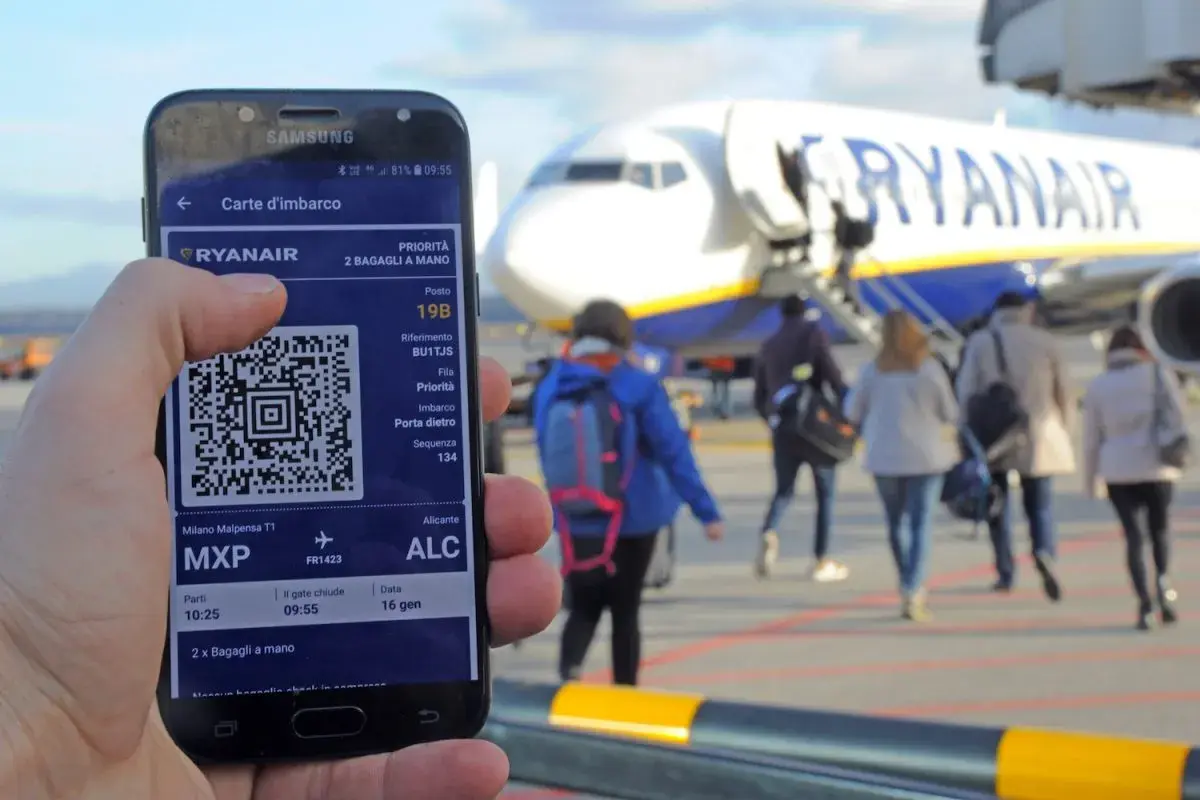 Ręka trzyma smartfon z kartą pokładową Ryanair. W tle samolot i pasażerowie.