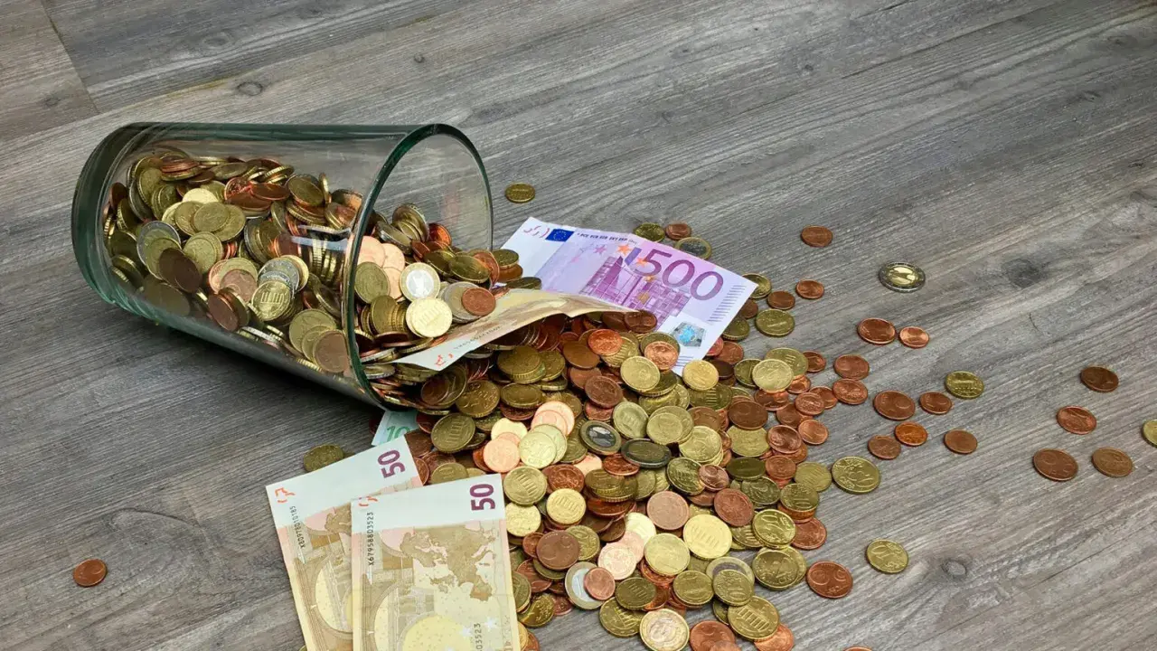 Słoik z monetami i banknotami, w tym 500 euro, rozsypany na drewnianej podłodze. To waluta Francji i innych krajów strefy euro.