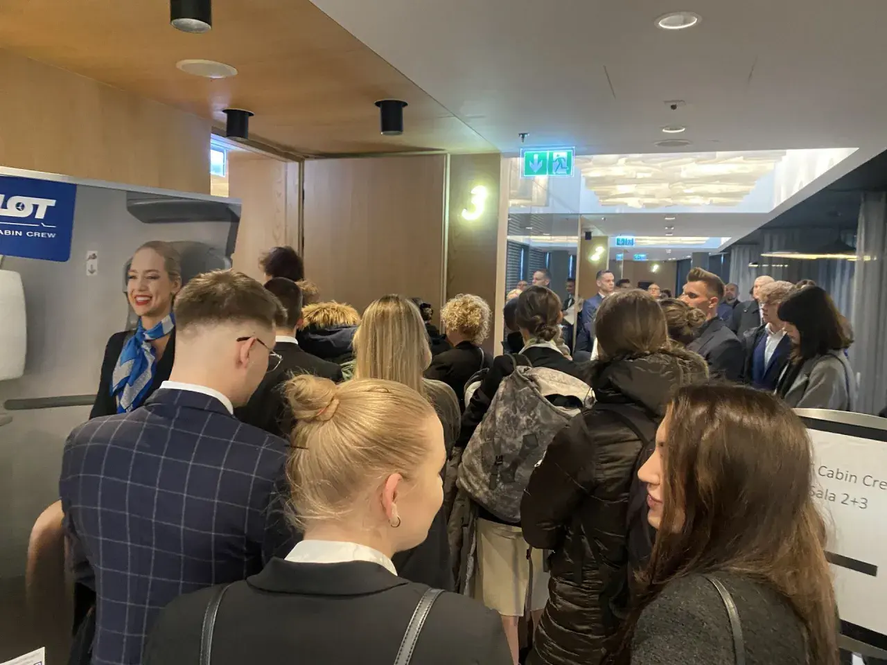 Uśmiechnięta stewardessa LOT Cabin Crew wita grupę osób. Marzenie o pracy w przestworzach zaczyna się tutaj.