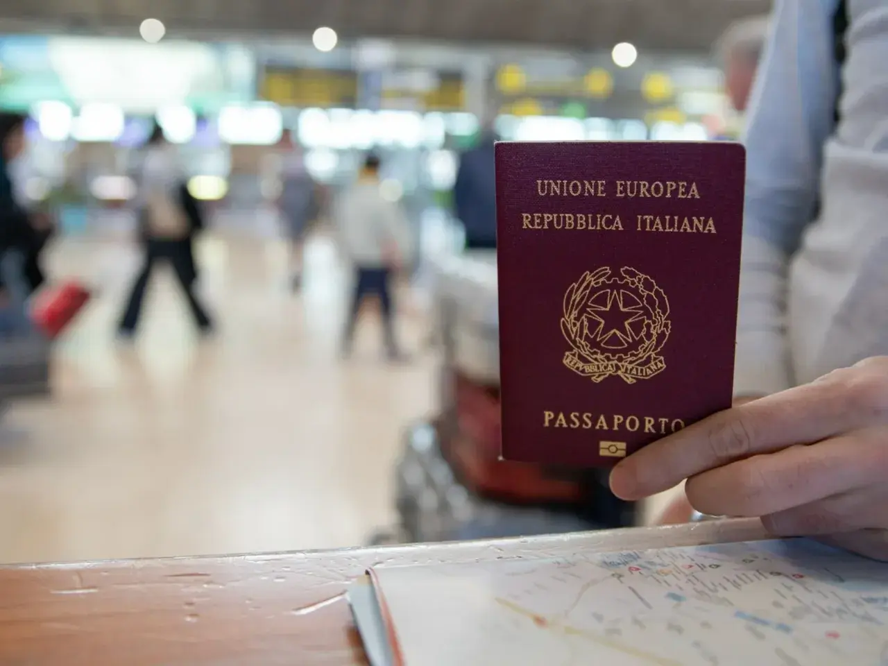 Włoski paszport w dłoni, na tle lotniska. Czy do Finlandii potrzebny jest paszport? Tak, jeśli nie jesteś obywatelem UE.