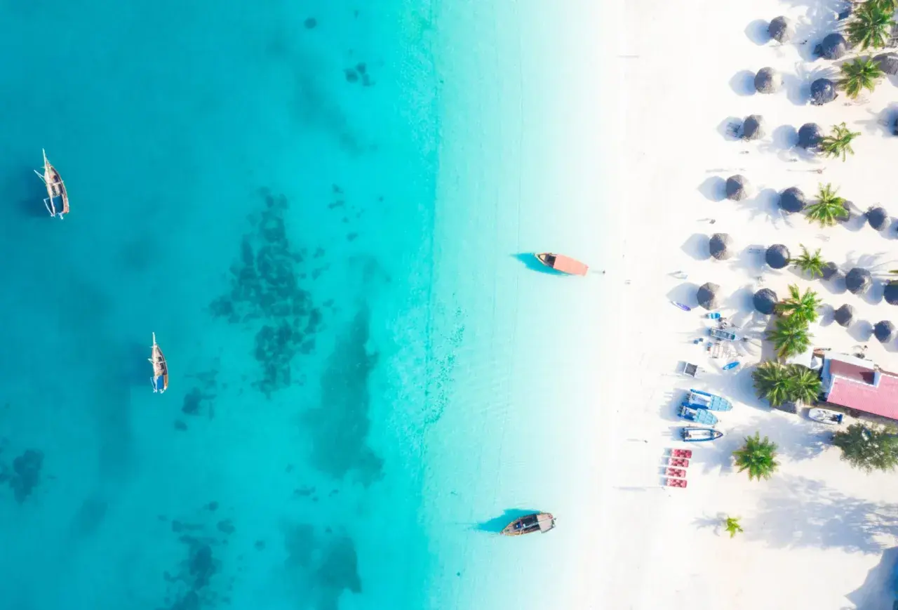 Rajska plaża na Zanzibarze, gdzie turkusowa woda i biały piasek tworzą idealne tło dla tradycyjnych łodzi. Można tu poczuć atmosferę wakacji, marząc o przygodach i wymieniając się wrażeniami, jakby to była lokalna waluta.