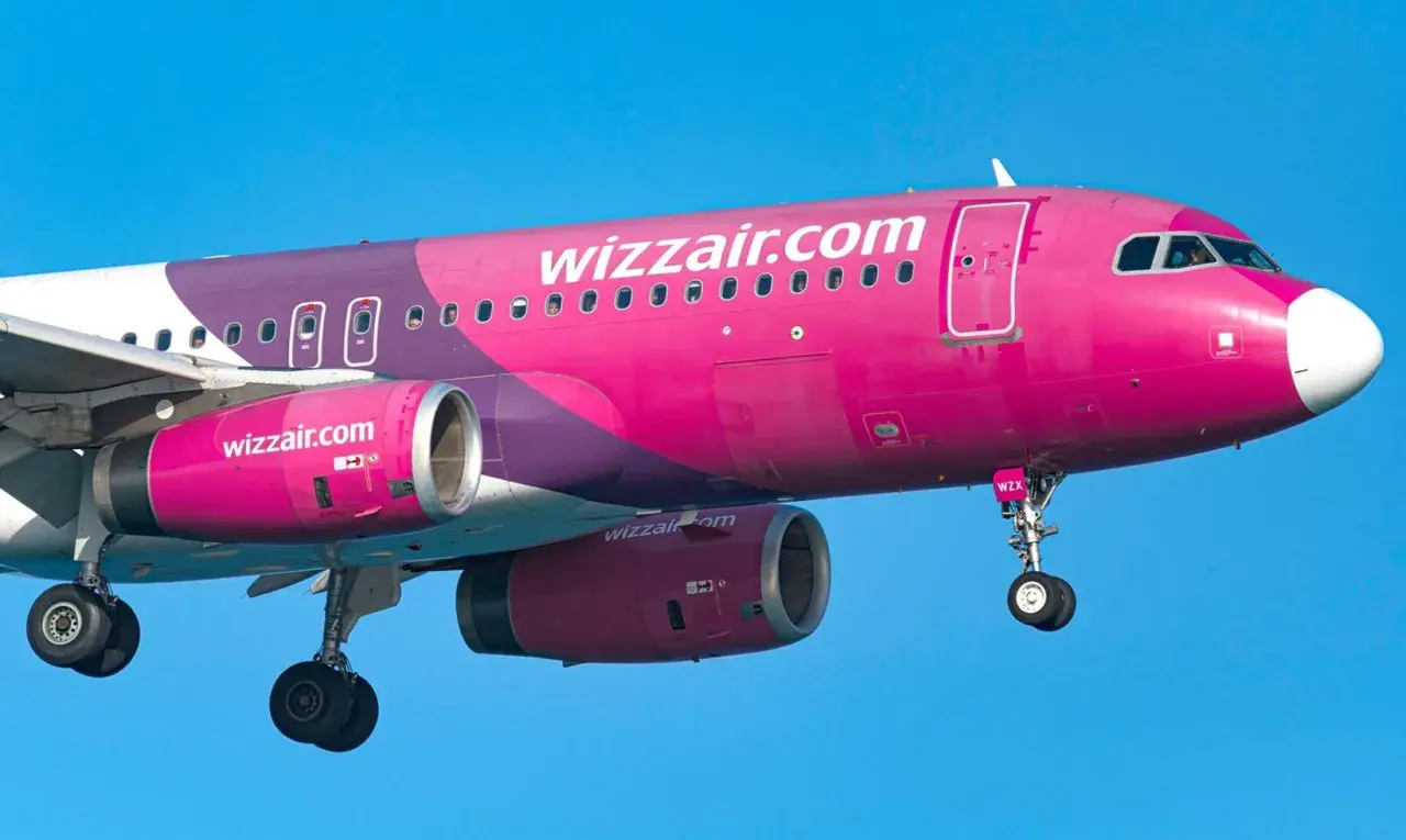 Różowy samolot Wizzair z fioletowymi elementami na tle błękitnego nieba.