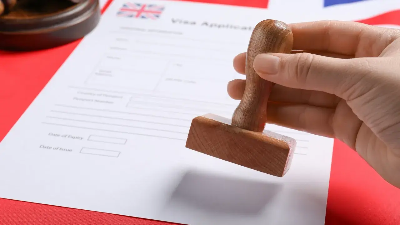 Dłoń trzyma pieczątkę nad formularzem wniosku o wizę do UK.