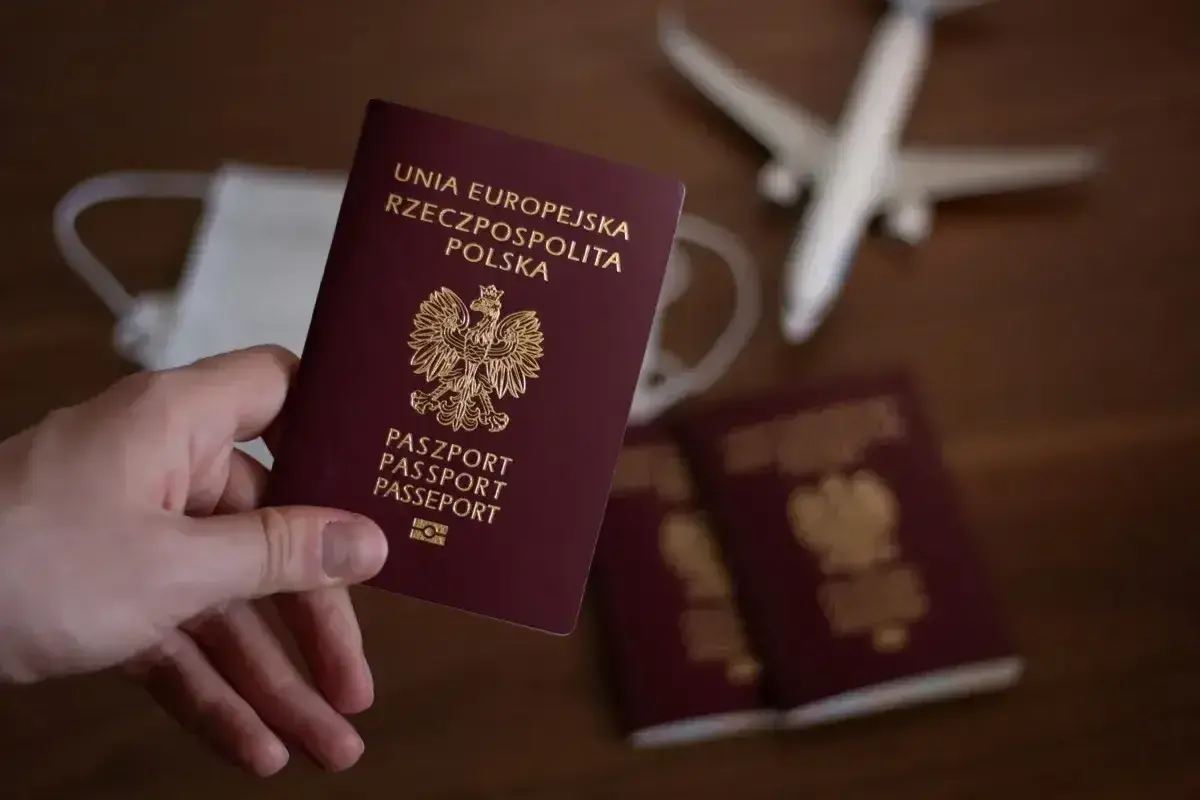 Dłoń trzyma polski paszport. Obok leżą kolejne dokumenty, maseczka i model samolotu. Zastanawiasz się, ile się czeka na paszport?