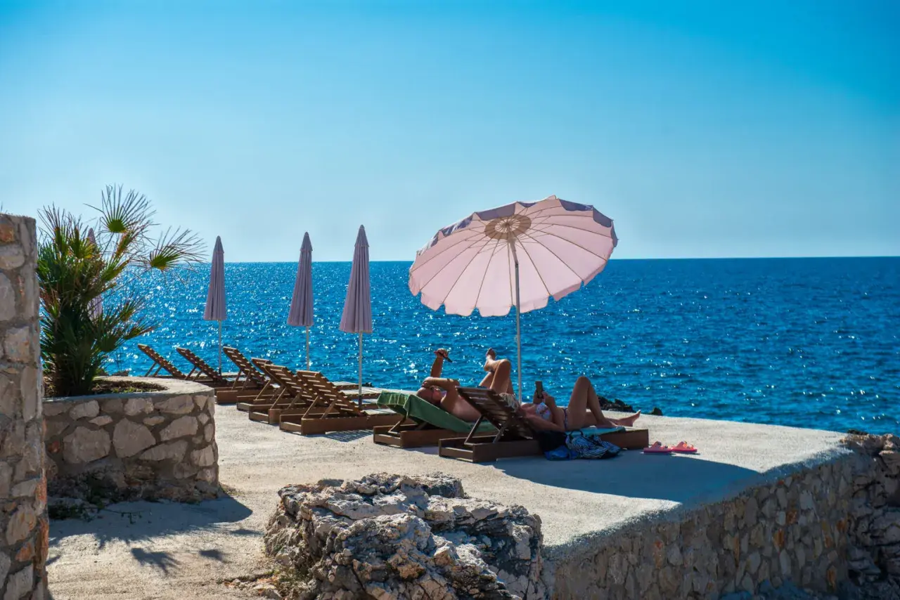 Relaks na plaży w Czarnogórze. Czy czarnogóra jest bezpieczna? Turyści odpoczywają na leżakach przy turkusowym morzu.