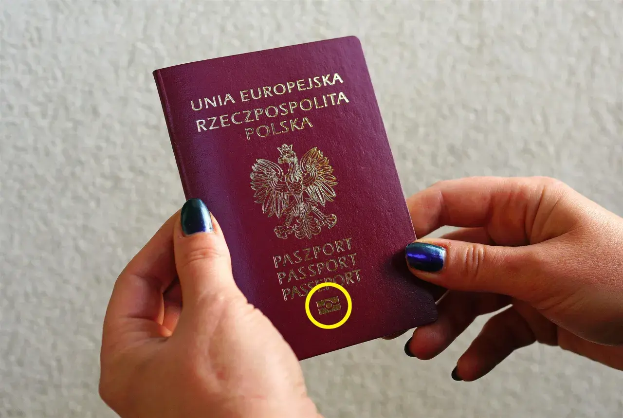Dłonie trzymają polski paszport biometryczny z symbolem aparatu.