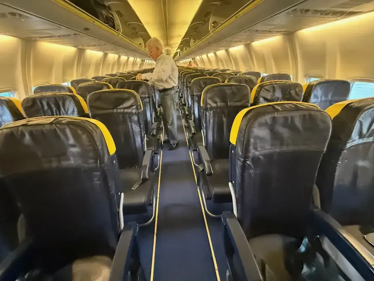 Wnętrze samolotu Boeing 737 z rzędami czarnych siedzeń z żółtymi zagłówkami. Zastanawiasz się, boeing 737 ile miejsc?