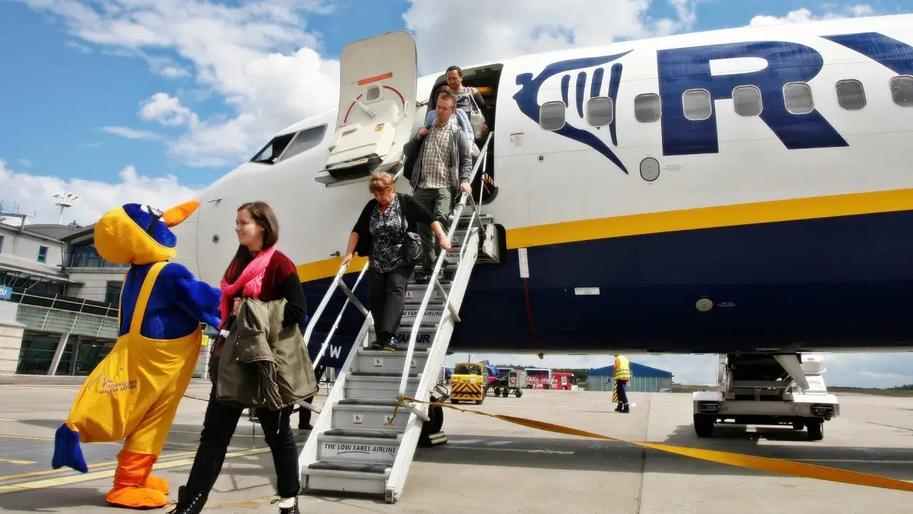 Ludzie schodzą po schodach z samolotu Ryanair, obok maskotka ptaka.