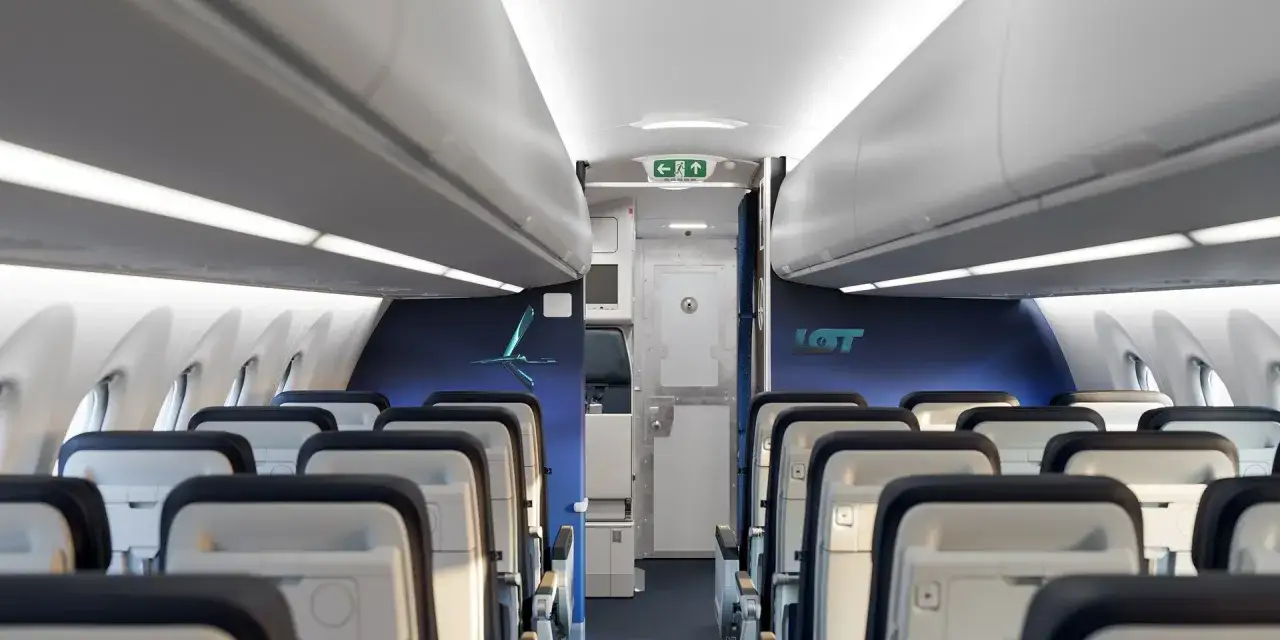 Wnętrze samolotu Airbus A220-300 LOT z rzędami białych foteli i niebieskimi ścianami.