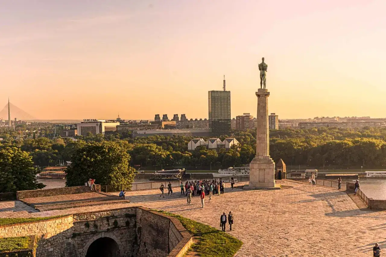Zachód słońca nad Belgradem, stolicą Serbii. Pomnik Zwycięzcy na tle panoramy miasta i rzeki.