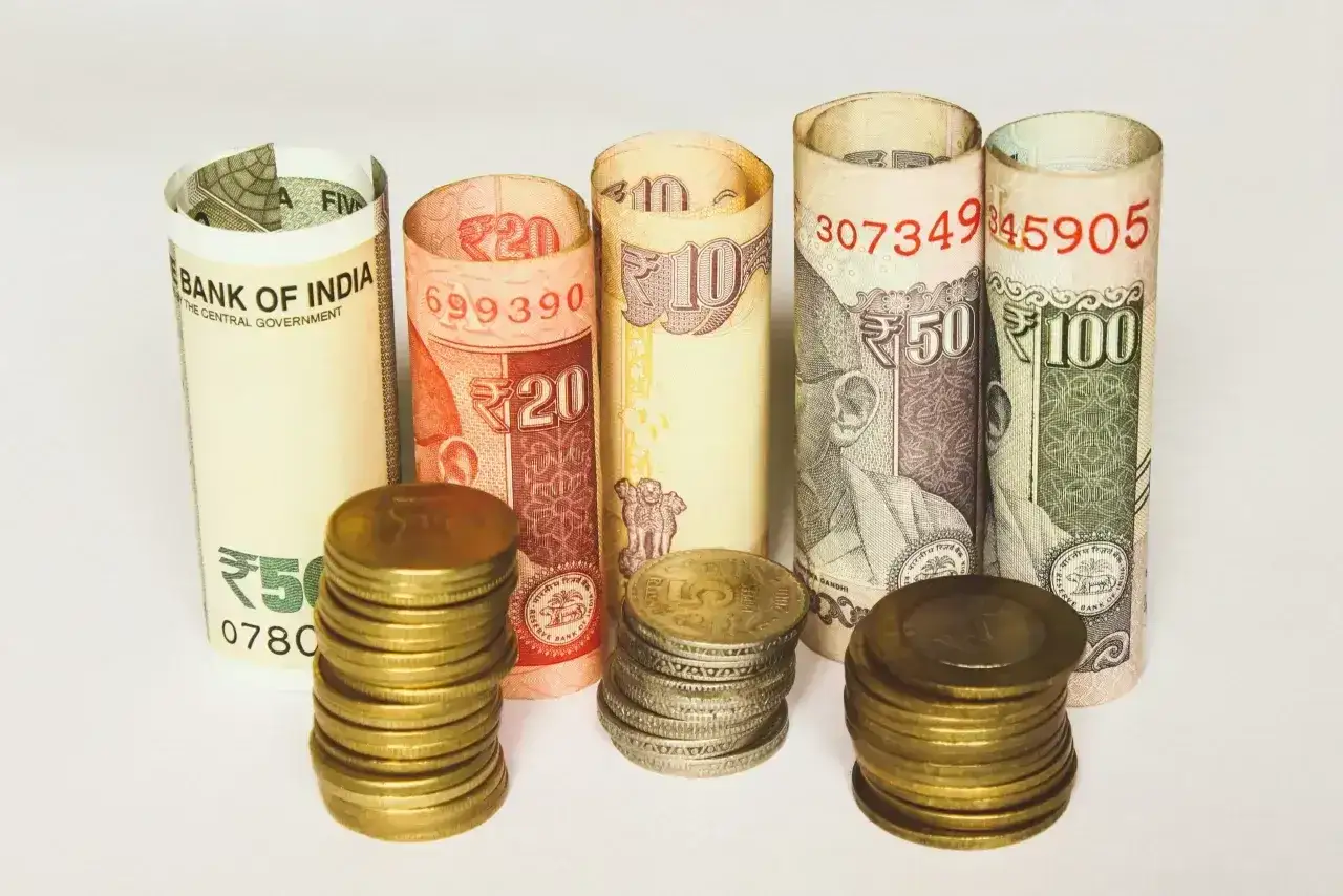 Indyjska waluta: zwinięte banknoty 5, 10, 20, 50, 100 rupii i stosy monet.